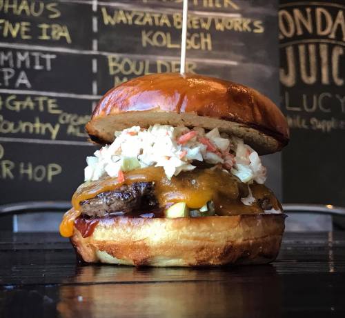 A close-up of a juicy cheeseburger with coleslaw on a toasted bun, set against a chalkboard menu backdrop.