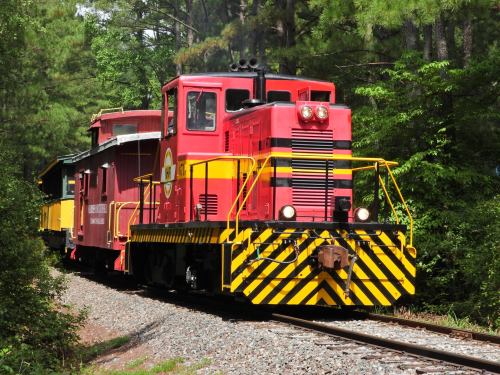 A bright red train engine with a yellow caboose on a gravel track surrounded by green trees.