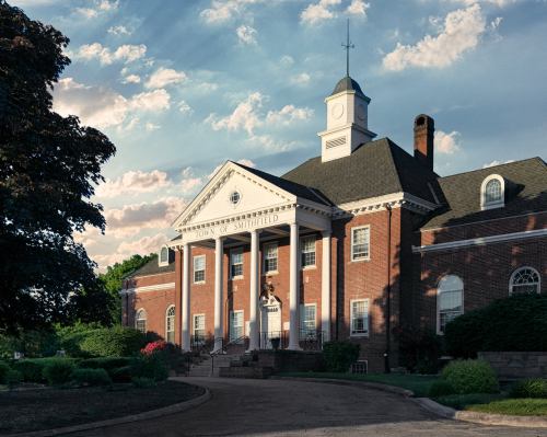 Historic brick town hall building with a clock tower, surrounded by greenery and a blue sky with clouds.