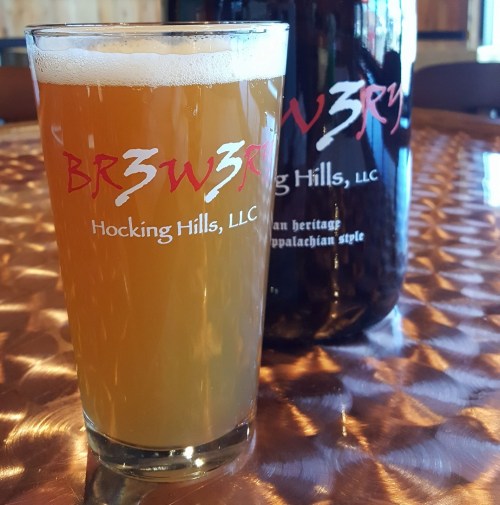 A glass of hazy beer next to a growler, both featuring the BR3W3RY logo from Hocking Hills, LLC.