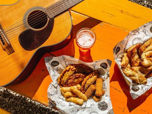A wooden guitar beside two baskets of fried snacks and a glass of beer on a bright orange table.