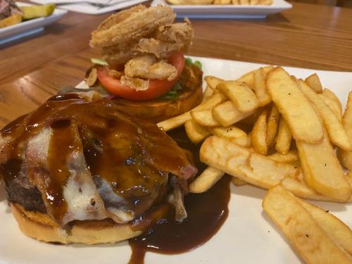 A juicy burger topped with barbecue sauce, bacon, and onion rings, served with a side of crispy French fries.