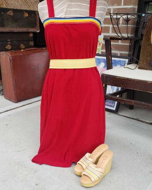 A red dress on a mannequin with a yellow belt, paired with beige wedge sandals, set against a vintage backdrop.