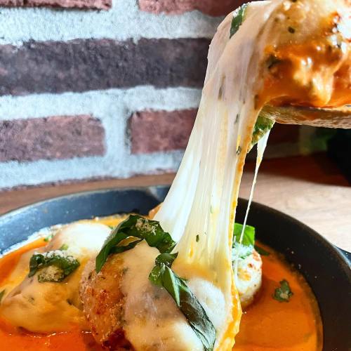 A close-up of cheesy pasta in a rich sauce, with fresh basil, being lifted from a skillet.