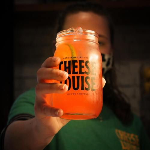 A person holds a jar of colorful drink with a slice of lime, featuring the logo of "Cheese House."