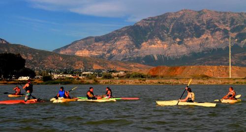 A group of kayakers paddles on a lake with mountains in the background under a clear blue sky.