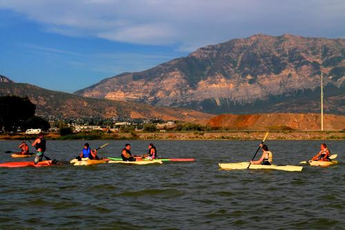 A group of kayakers paddles on a lake with mountains in the background under a clear blue sky.