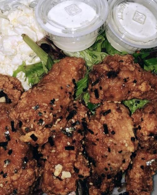 A close-up of crispy fried chicken wings on a bed of greens, accompanied by two small containers of dipping sauce.