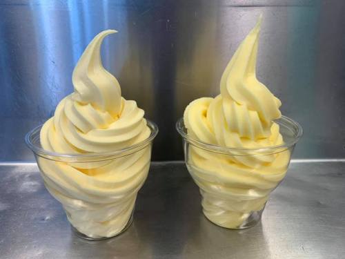 Two cups of soft-serve ice cream with a creamy, swirled texture, set against a metallic background.