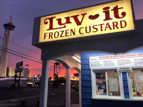 A brightly lit sign for "Luv-it Frozen Custard" against a colorful sunset, with a tower in the background.