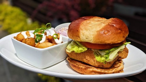 A crispy chicken sandwich with lettuce and tomato, served with a side of seasoned potato bites and dipping sauce.