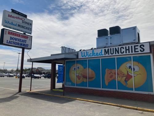 Exterior of Wicked Munchies restaurant with a colorful sign and cartoon food images, located in a shopping area.