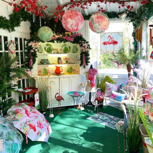 A vibrant shop interior decorated with tropical plants, flamingo decor, colorful umbrellas, and floral accents.