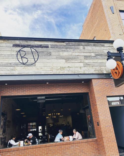 A cozy restaurant with a wooden exterior and a logo, featuring diners enjoying their meals at outdoor tables.