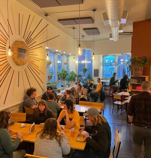 A cozy restaurant interior with patrons enjoying meals at wooden tables, surrounded by plants and warm lighting.
