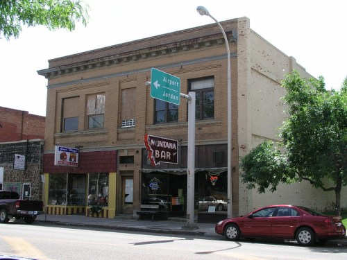 A two-story brick building with a bar sign, street signs for Airport and Jordan, and parked cars in front.