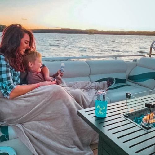 A woman and a child sit together on a boat, wrapped in blankets, enjoying a sunset over the water.
