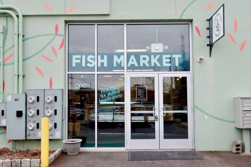 Exterior of a fish market with large glass doors, "FISH MARKET" sign, and colorful wall design. Open for business.