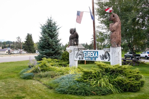 Welcome sign for Eureka, Montana, featuring carved bear sculptures and flags, surrounded by greenery.