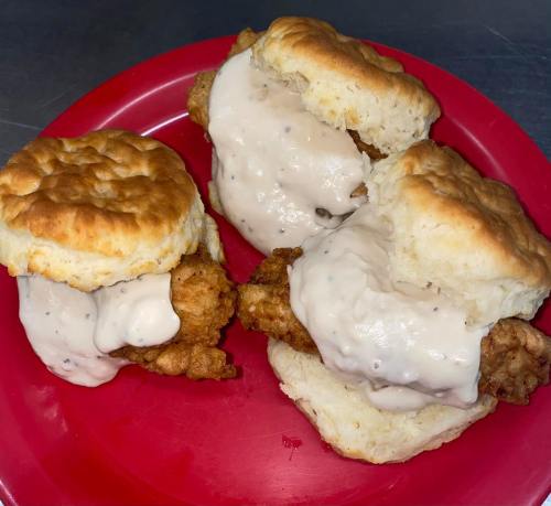 Two fried chicken biscuits topped with creamy gravy on a red plate.
