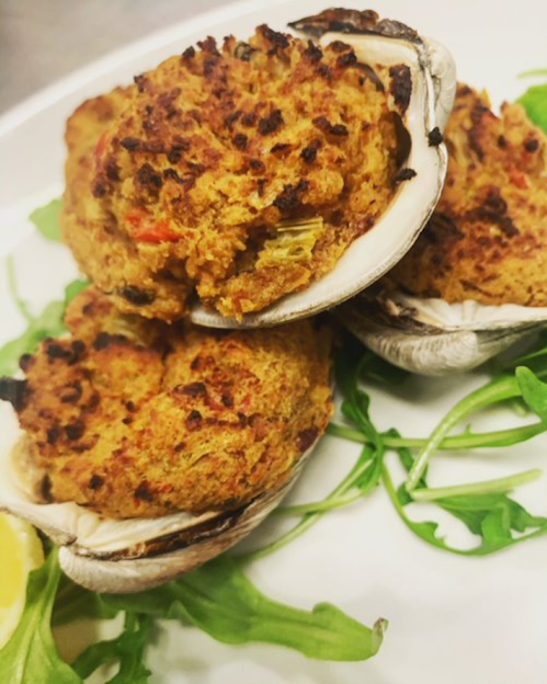 Three stuffed clams on a plate, garnished with arugula and a lemon wedge.