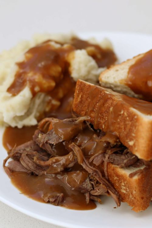 A plate featuring a beef sandwich with gravy, served alongside mashed potatoes topped with more gravy.