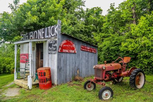 A rustic building with a sign reading "Big Bone Lick" and an old red tractor parked outside, surrounded by greenery.