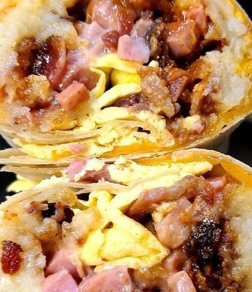 Close-up of a halved burrito filled with scrambled eggs, ham, and crispy bits, showcasing a savory, hearty filling.