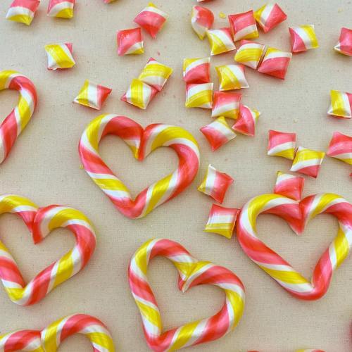 Colorful heart-shaped candy canes and small square candies scattered on a light background.