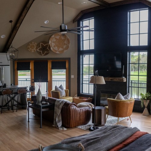 Cozy living room with large windows, modern furniture, and a view of nature, featuring a mix of textures and warm colors.