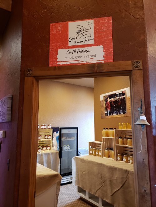 Entrance to Cox's Farm Stand in South Dakota, featuring shelves of products and a cooler in a cozy interior.