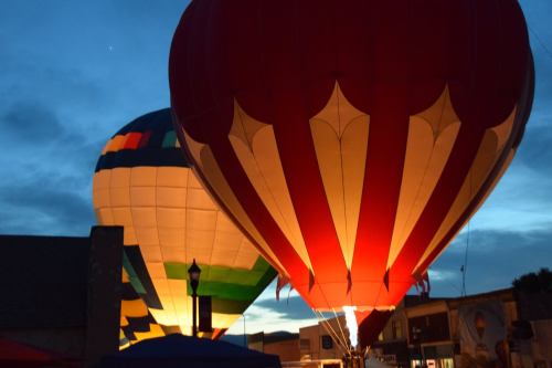 Two colorful hot air balloons illuminated against a twilight sky, with one balloon featuring red and white stripes.