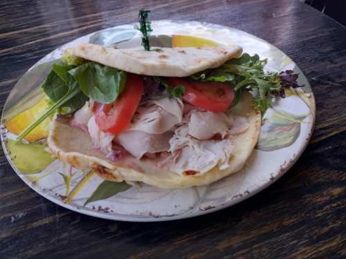 A plate with a flatbread sandwich filled with turkey, lettuce, and tomato, garnished with a sprig of green.