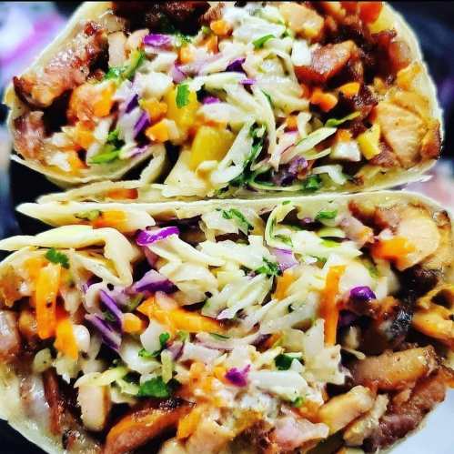 Close-up of a halved burrito filled with grilled meat, colorful vegetables, and creamy sauce.