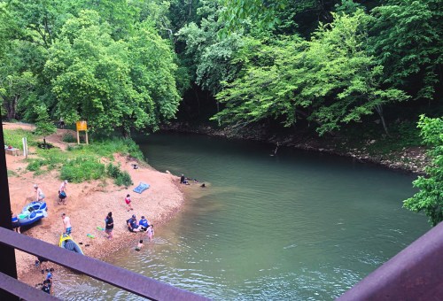A serene river scene with people enjoying the water, surrounded by lush green trees and sandy banks.