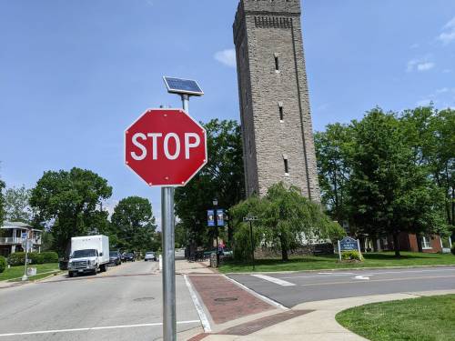 A stop sign in front of a tall stone tower, with trees and a clear blue sky in the background.