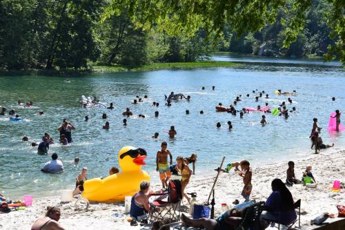 A busy beach scene with people swimming, a large inflatable duck, and children playing by the water under sunny skies.