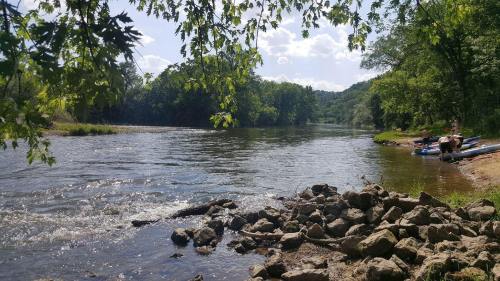 A serene river scene with rocky banks, lush greenery, and people enjoying kayaking under a sunny sky.