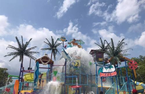 A colorful water park structure with slides, palm trees, and a large splash feature under a blue sky.