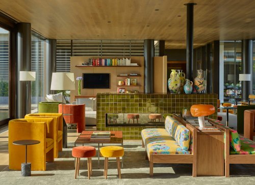 A modern living room with colorful furniture, a green tiled fireplace, and large windows letting in natural light.