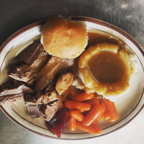 A plate of sliced roast beef with gravy, mashed potatoes, carrots, and a roll.