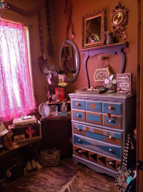 A cozy room corner featuring a colorful dresser, vintage decor, and a window with pink curtains.