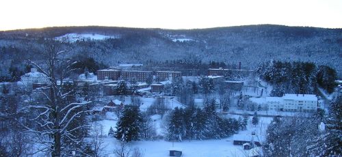 A snowy landscape with a large building surrounded by trees and hills, bathed in soft winter light.