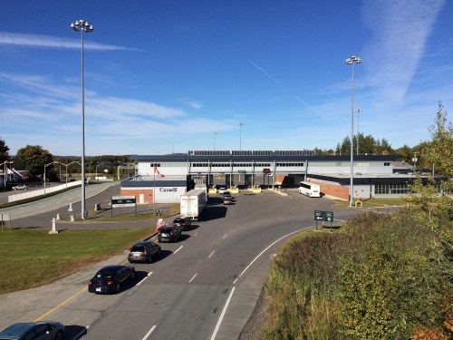 A border crossing station with vehicles lined up, under a clear blue sky and surrounded by greenery.