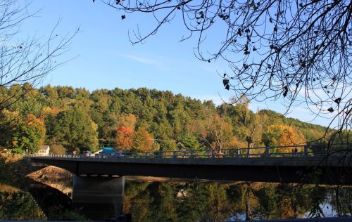 A bridge spans a river, surrounded by colorful autumn trees under a clear blue sky.