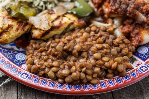 A colorful plate featuring lentils, grilled chicken, and mixed vegetables on a decorative border.