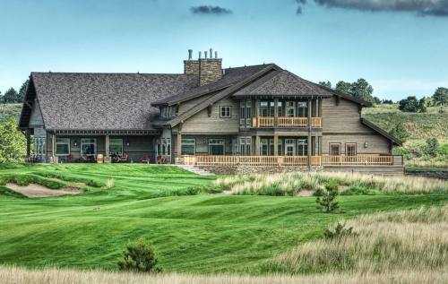 A large, modern house with a wooden exterior, surrounded by green grass and a golf course landscape.