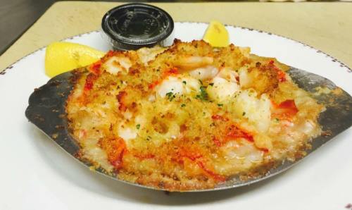 Baked seafood dish with shrimp, topped with golden breadcrumbs, served with lemon wedges and a side of sauce.