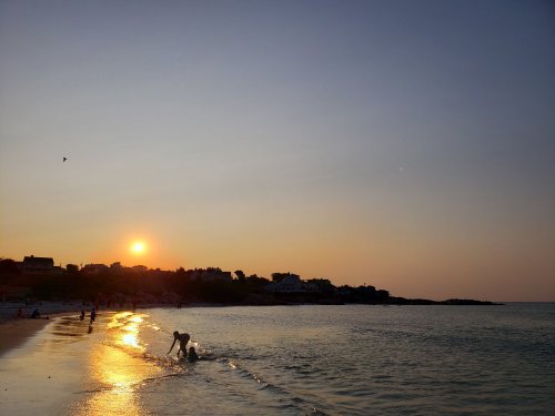 A serene beach at sunset, with silhouettes of people playing in the water and a warm glow reflecting on the sand.