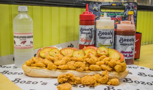 A large sub filled with fried seafood, accompanied by condiments and a bottle of water on a branded table.